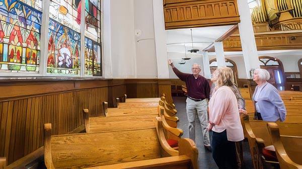 A group of older adults visiting a church, admiring stained glass windows.