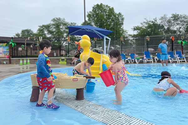 Toddlers wearing colorful bathing suits, playing in shallow water in Gouin Swimming Pool