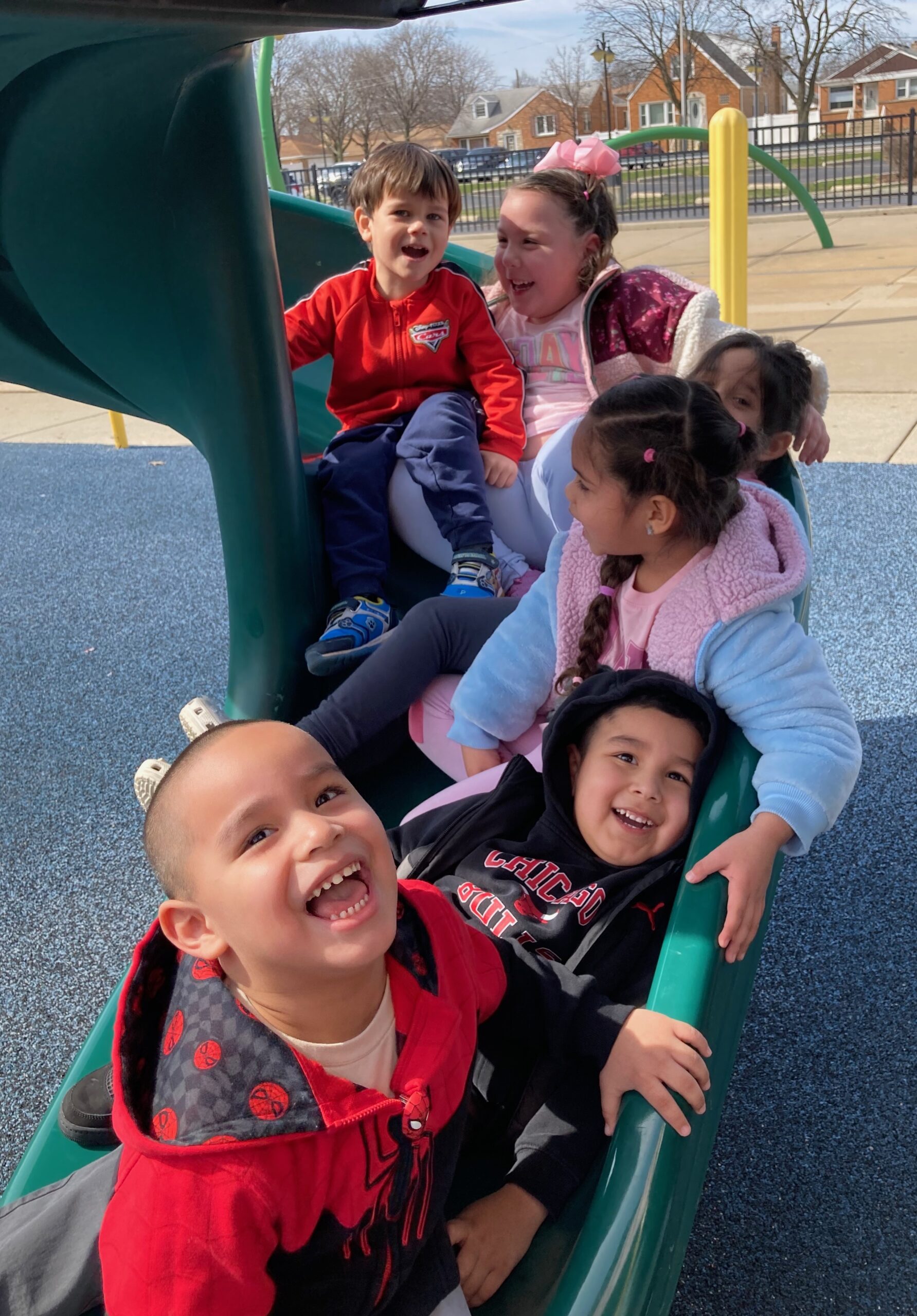 A group of preschool-age kids going down a slide at the park, laughing.